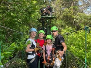 Gezin met helmen en klimgordels staat op een hangbrug in het regenwoud van Costa Rica, klaar voor een zipline-avontuur.