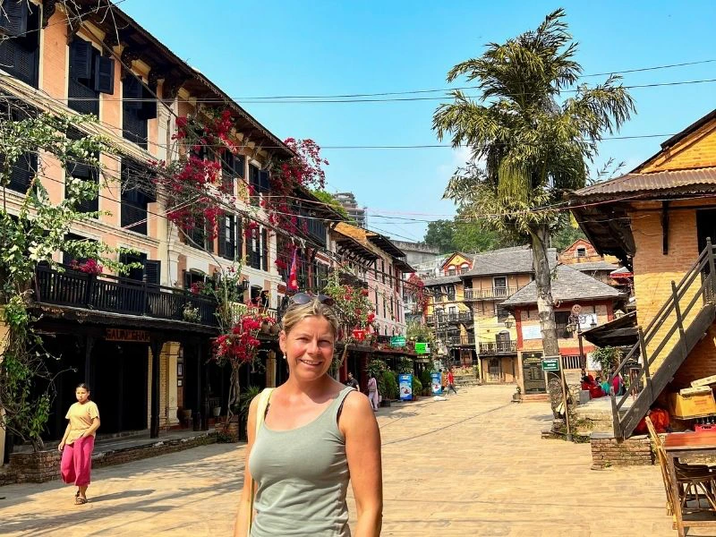 Vrouw loopt door een straat met huisjes en bloemen in Nepal