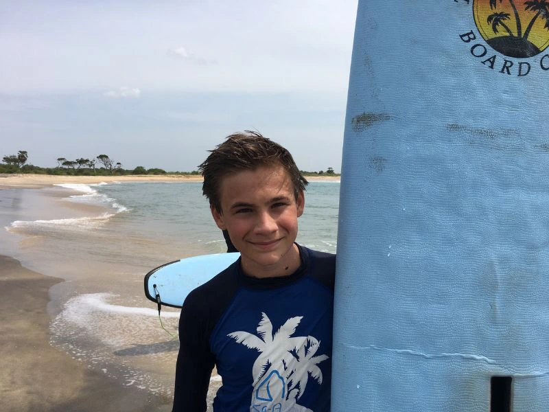 Jongen staat op het strand met een surfplank in zijn hand.