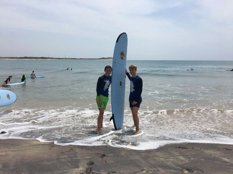 Twee jongens staan met een surfboard op het strand.