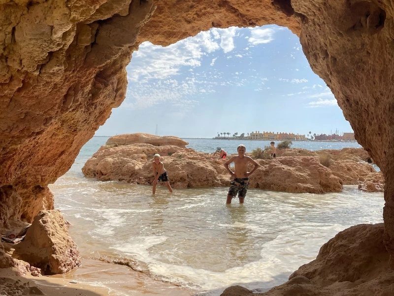 2 jongens staan in in water in de Algarve. Vlakbij het strand en kijken door een rotsformatie