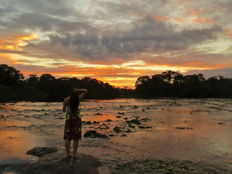 Vrouw staat bij zonsondergang bij een rivier in Suriname