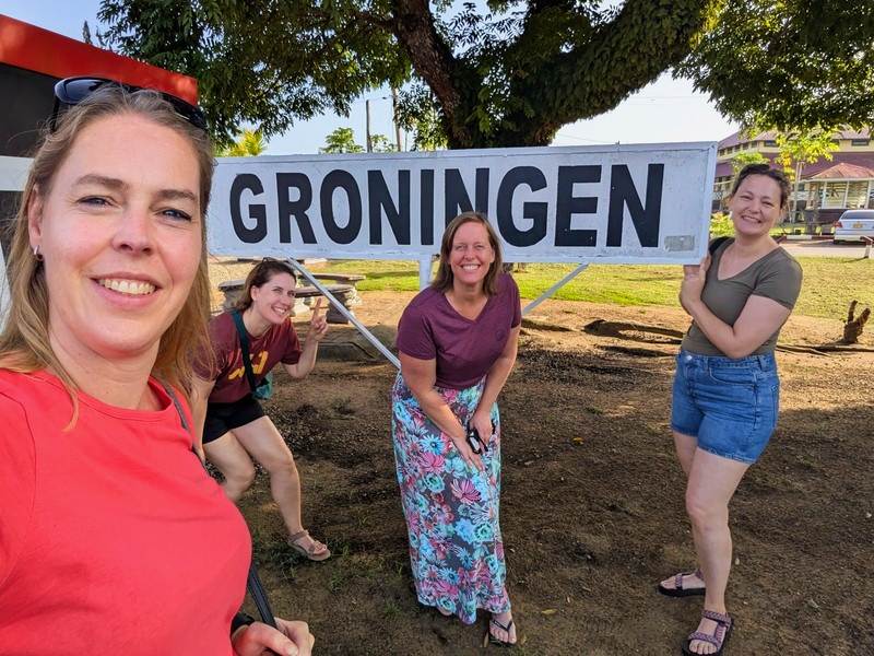 Reizigers bij het bord van Groningen in Suriname