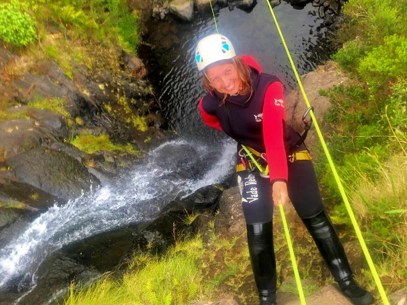 Vrouw in klimuitrusting en wetsuit abseilt langs een rotswand bij een waterval.