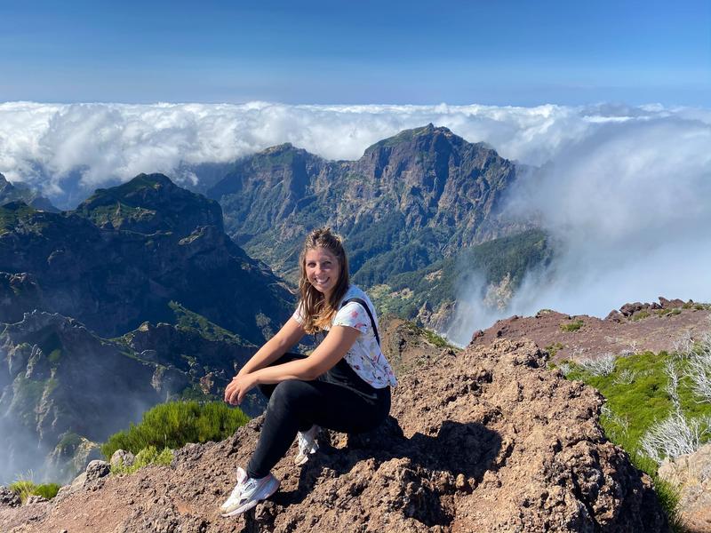 Vrouw zit op een rots met uitzicht over groene bergen en wolkenzee op de achtergrond.