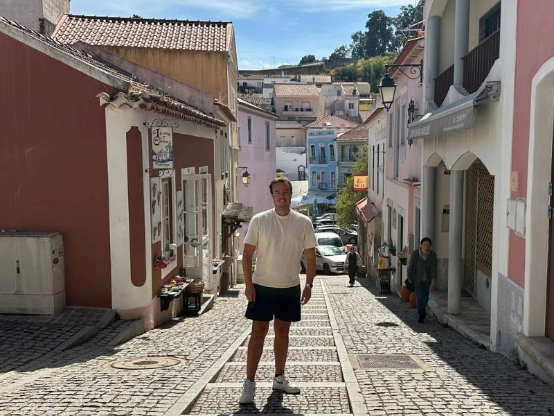 Man staat in een smalle geplaveide straat met kleurrijke huizen in een heuvelachtig stadje.
