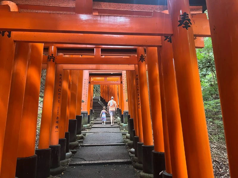 Vader met dochtertje hand in hand op de trappen van de Fushimi Inari-taisha met zijn rood gekleurde palen en Japanse tekens erop.