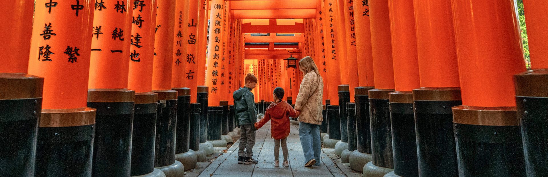 Moeder met kinderen tussen rode torii-poorten in Kyoto