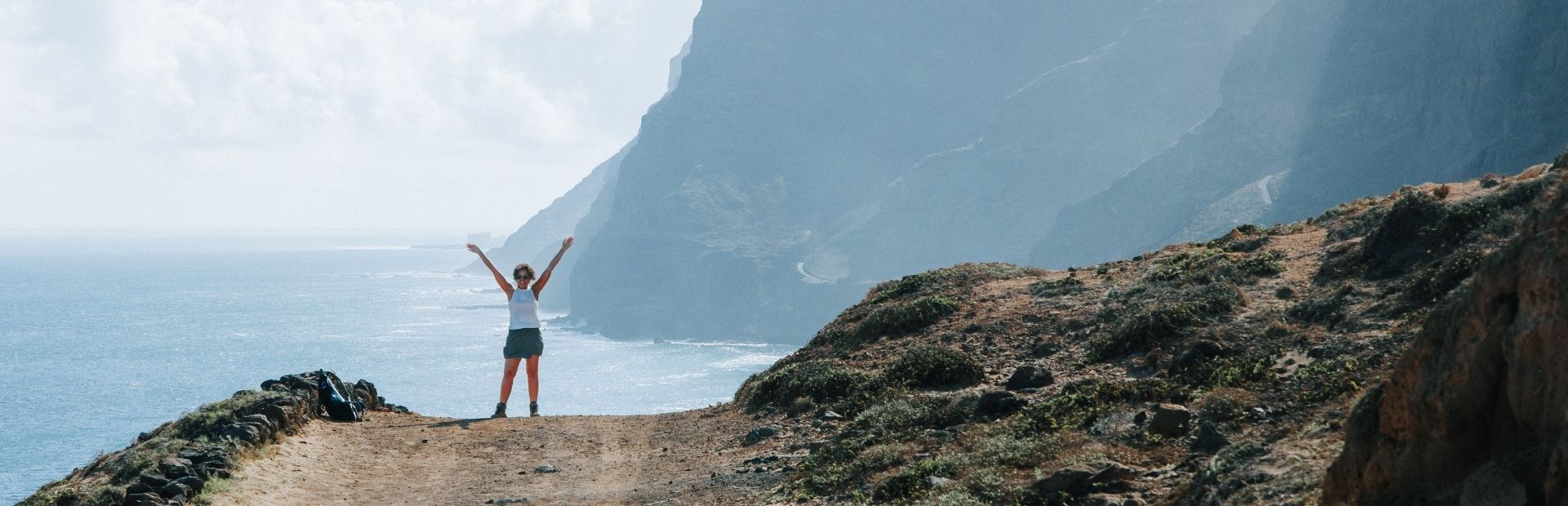 Vrouw staat op een weg aan het water met kliffen op de achtergrond