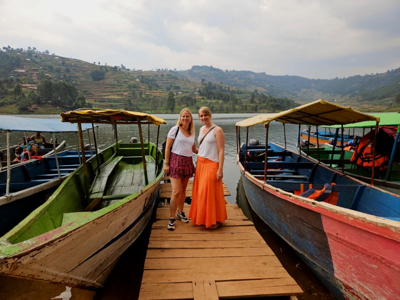 Vrouwen poseren aan het water met boten bij Lake Bunyonyi