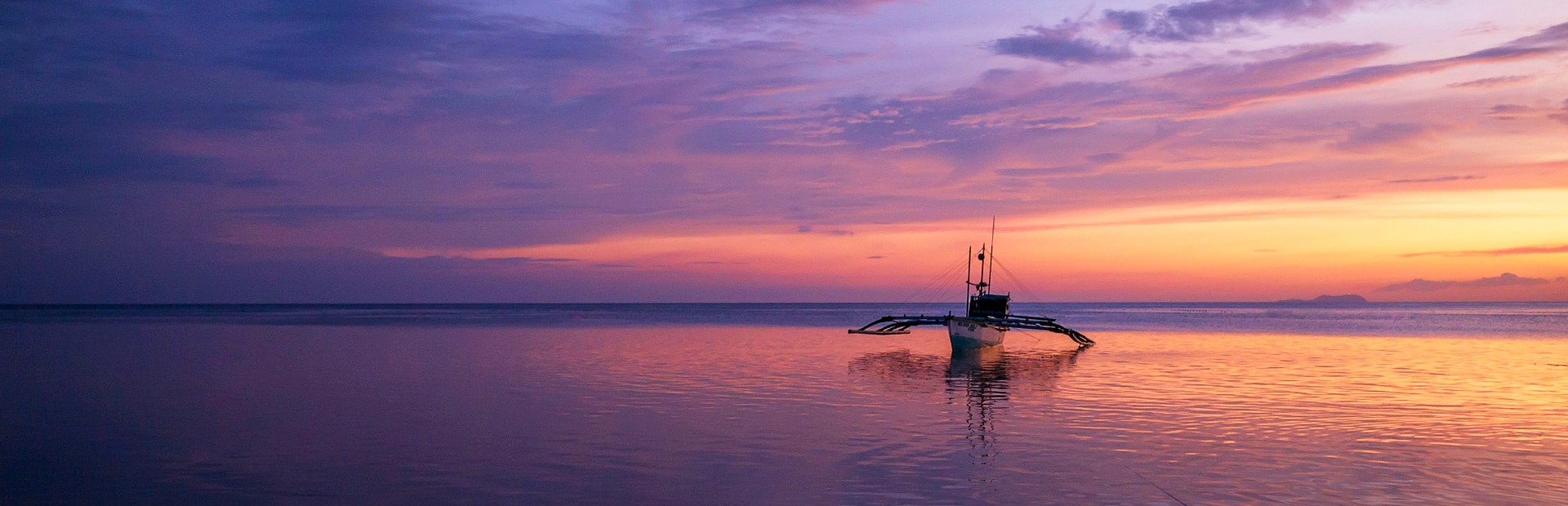 Ondergaande zon op Siquijor met een traditionele Filipijnse boot in de branding terwijl de lucht kleurt van paars naar geel