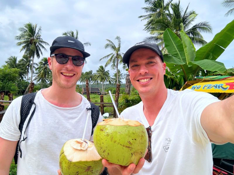 twee mannen met een pet op die een verse kokosnoot in de hand houden