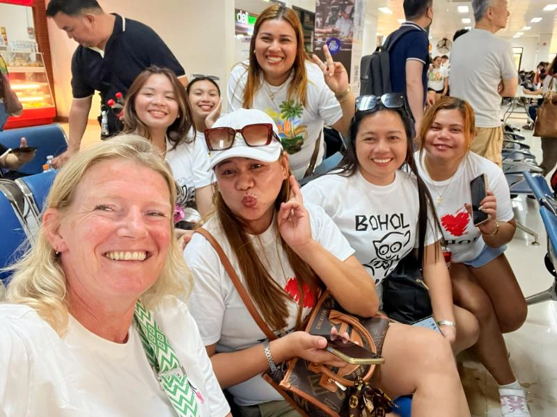 blanke vrouw te midden van filipijnse vrouwen die een selfie maken en allemaal in de camera kijken terwijl ze wachten op de ferry met op de achtergrond andere mensen